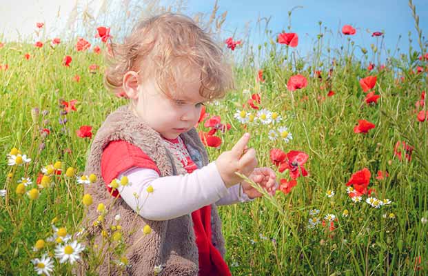 Kind sitzt auf einer Blumenwiese